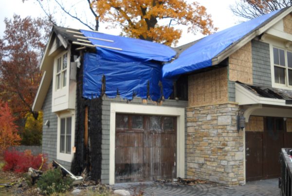 A blue tarp covering the roof of a house undergoing cleaning to remove soot and smoke damage.