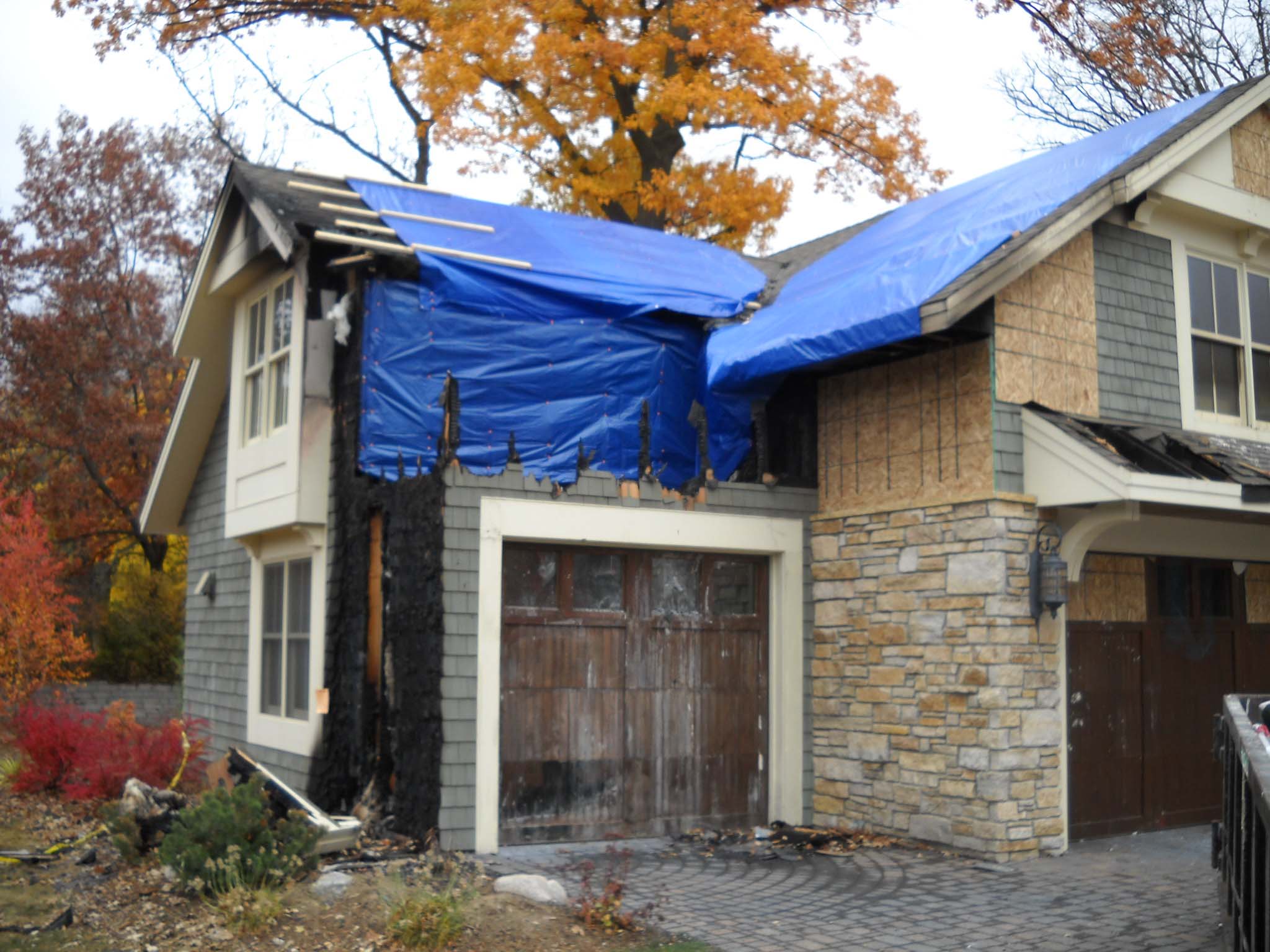 A blue tarp covering the roof of a house undergoing cleaning to remove soot and smoke damage.