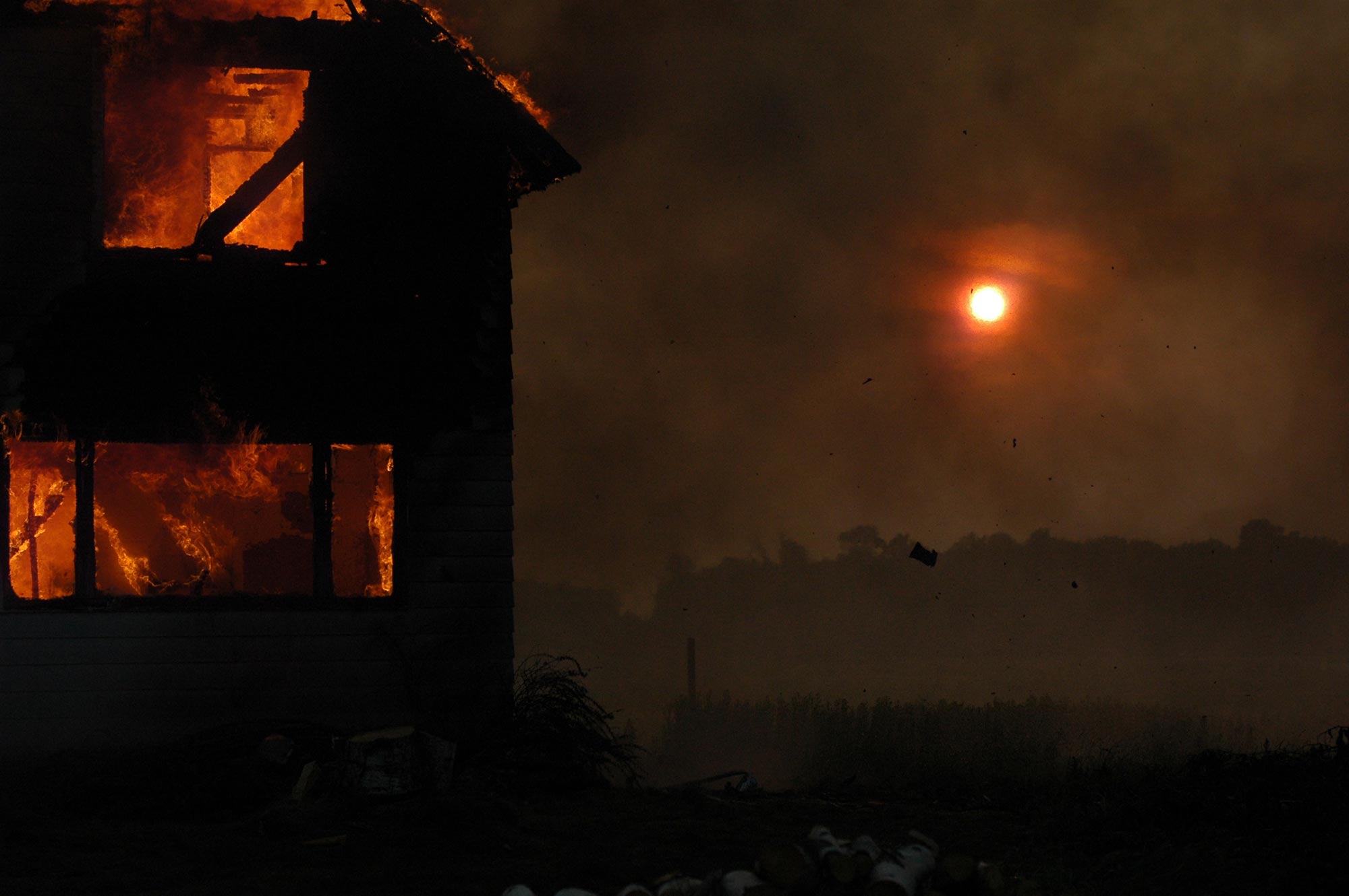 A house is engulfed in flames, causing severe fire damage in the middle of a field.