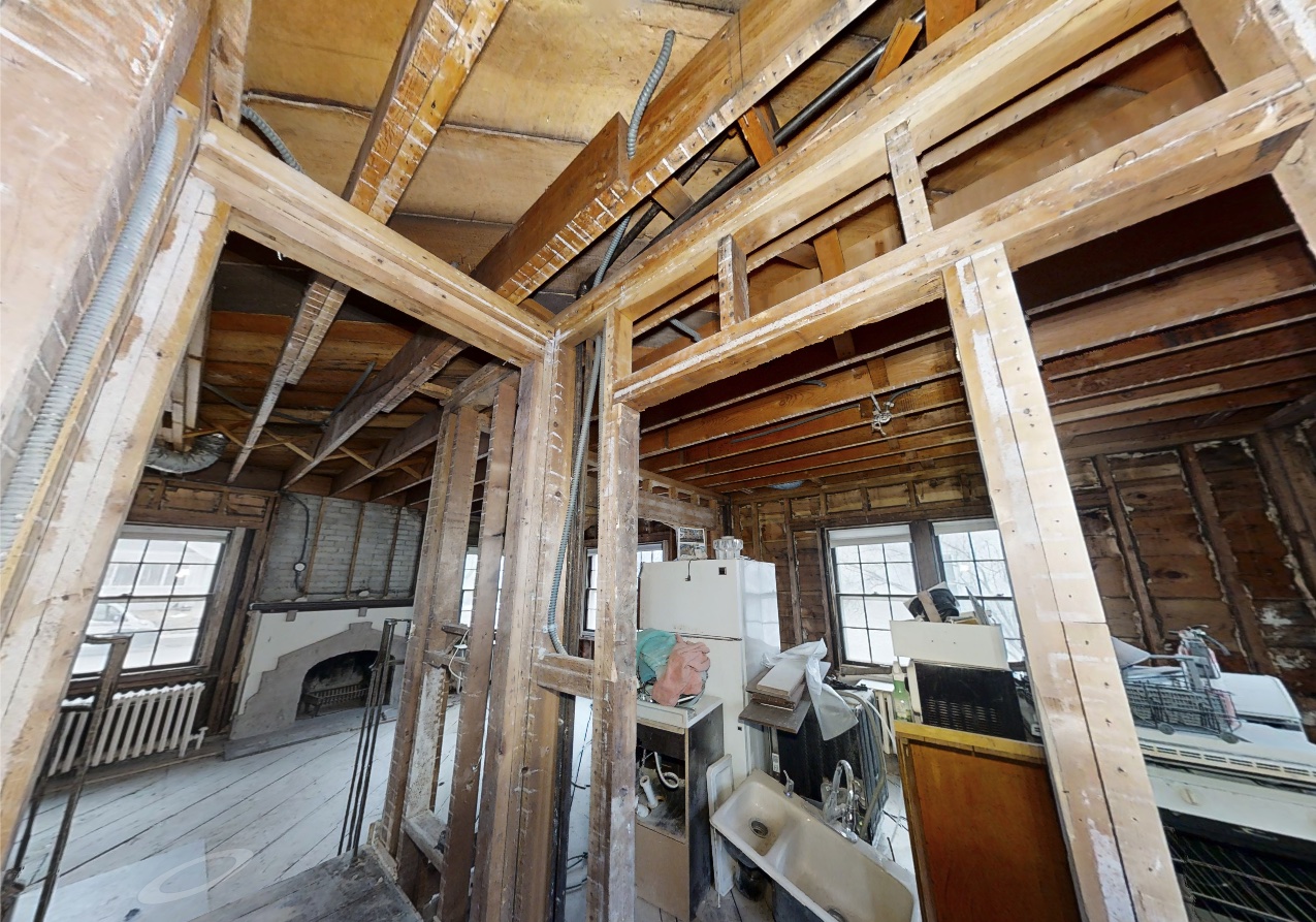 Interior of a Minneapolis home restoration, showing exposed wooden framing, electrical wiring, and construction materials. Windows provide natural light to the space, revealing progress in repairing the damage from a past boiler fire.