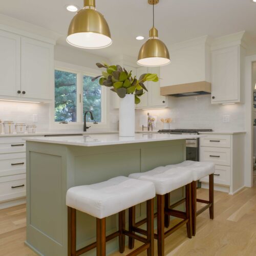A modern kitchen with white cabinetry, a central island with stools, large gold pendant lights, and a view into a dining area with patterned wallpaper shines after an expert Edina water damage remodel.