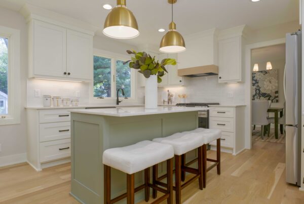A modern kitchen with white cabinetry, a central island with stools, large gold pendant lights, and a view into a dining area with patterned wallpaper shines after an expert Edina water damage remodel.